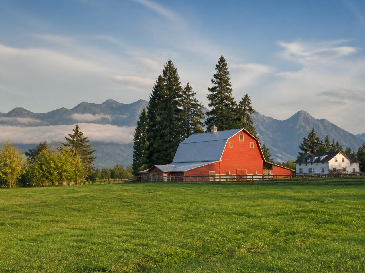 A red barn and farmhouse on a Fraser Valley farm with mountains behind, British Columbia
